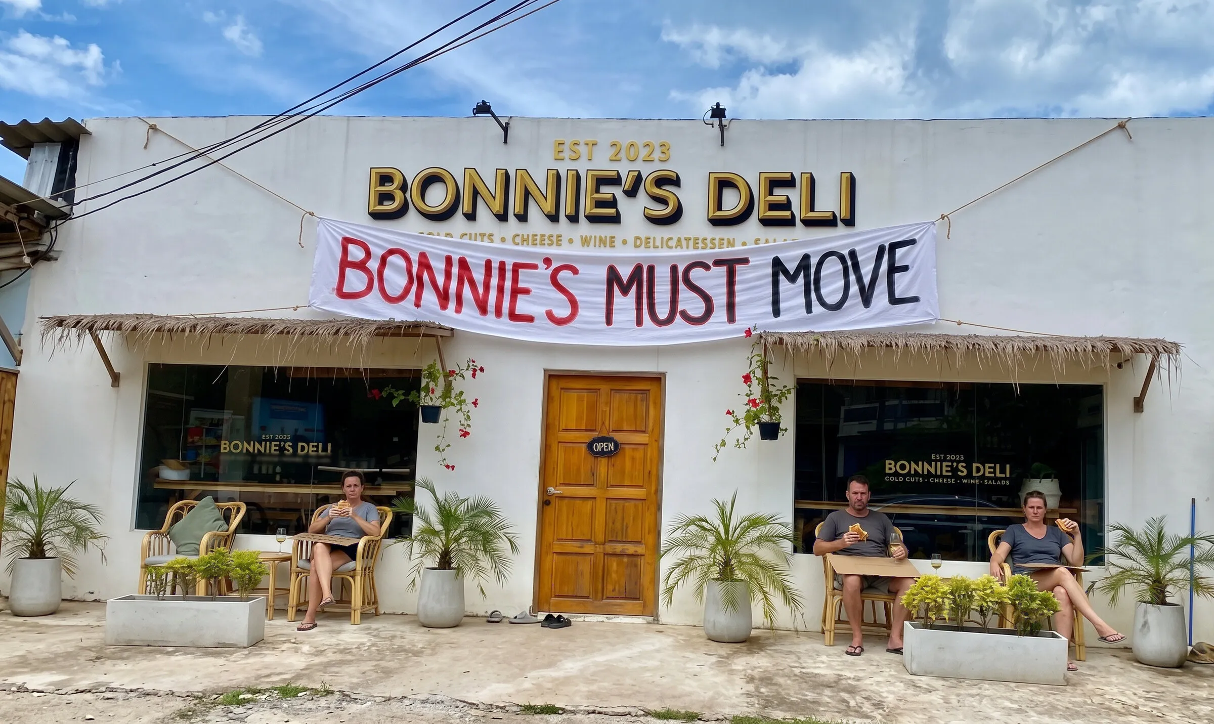 A bedsheet banner reading Bonnie's must move hung across the front of Bonnie's Deli, with protesters eating in the chairs below